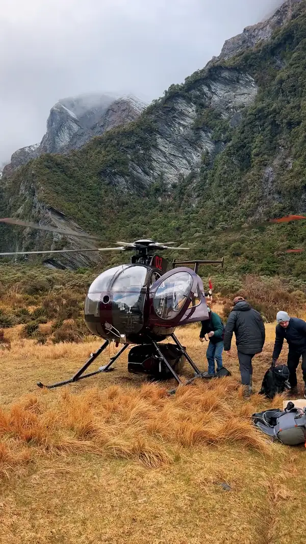 The helicopter on a tussock flat, unloading gear below the peaks
