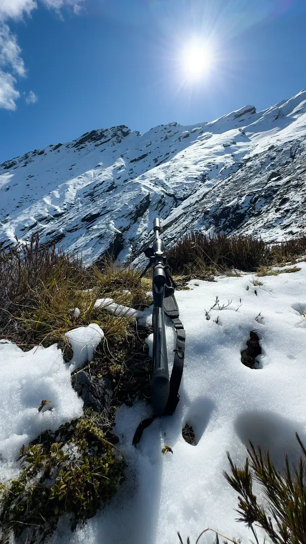 A rifle resting in the snow on the tops