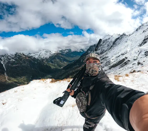 On a snow covered ridge with a suppressed rifle, the valley falling away behind