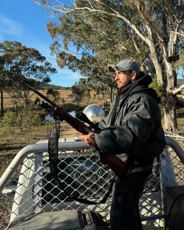 On the back of the ute with a rifle and the spotlight at last light